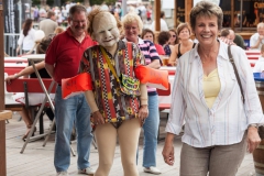 Maskenfigur geht mit Bademantel und Schwimmflügel spazieren, Zuschauer lachen