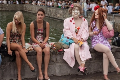 Zwei Maskenspielerinnen sitzen draußen mit Bademantel und Badehose, daneben zwei junge Frauen